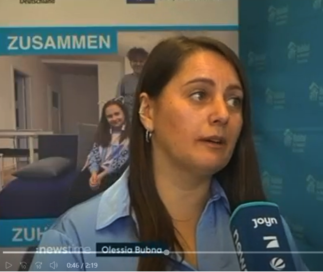 Standbild aus dem :newstime-Beitrag: Interview vor einer „Zusammen Zuhause schaffen“-Fotowand