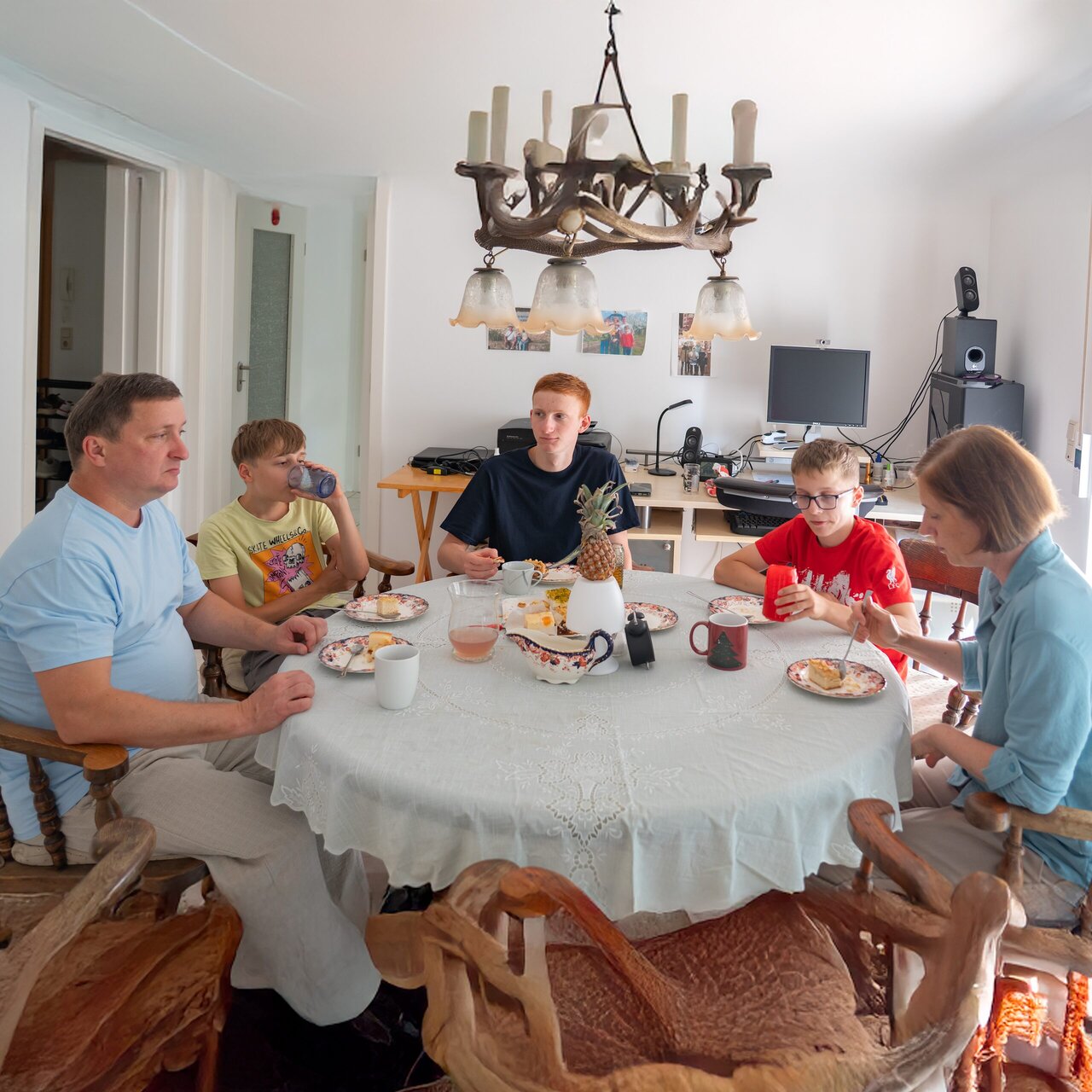 Eine Familie mit drei Jugendlichen sitzt gemeinsam an einem runden Esstisch beim Essen.