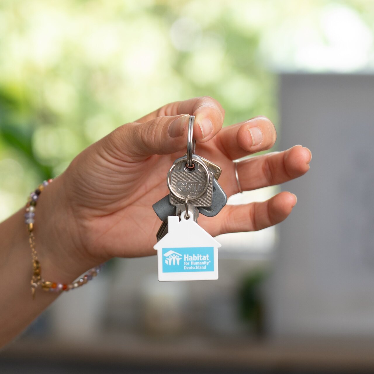 An open hand holds a bunch of keys with a house-shaped Habitat key ring.